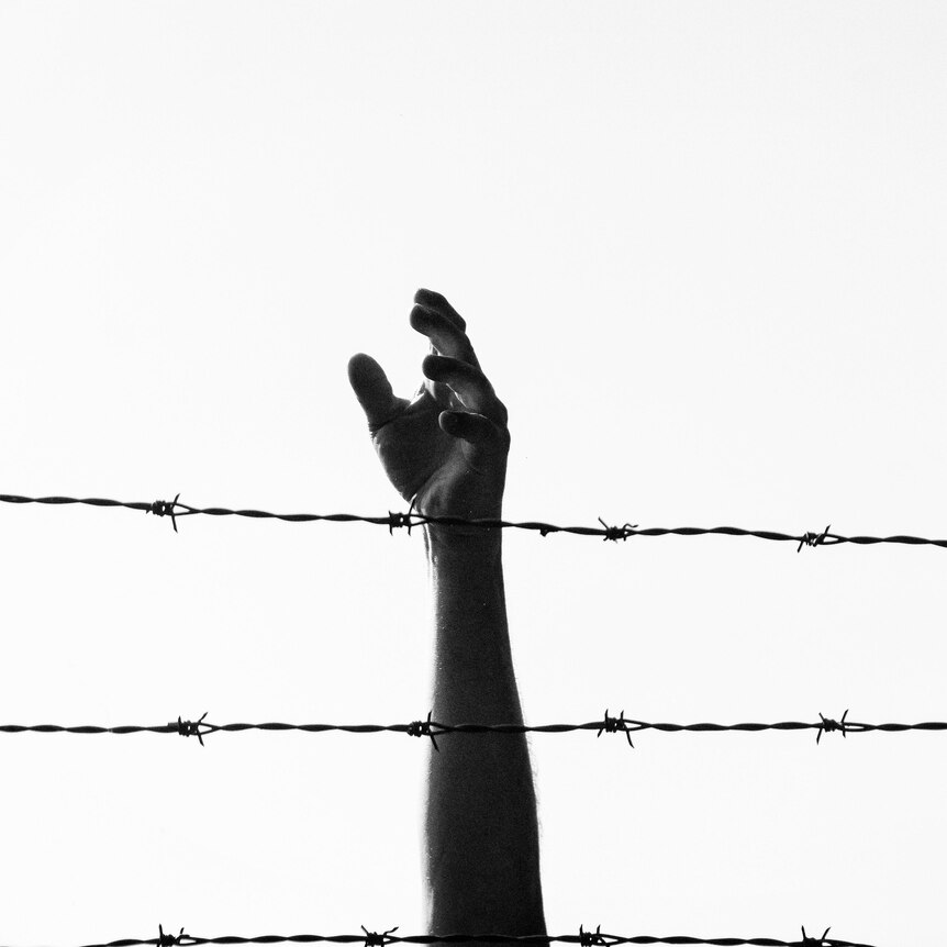Hand reaching up behind barbed wire and fence