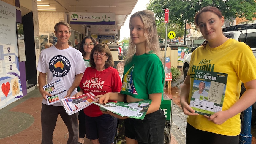 Volunteers in brightly coloured tee shorts hand out how-to-vote pamphlets outside a pre-poll voting booth.