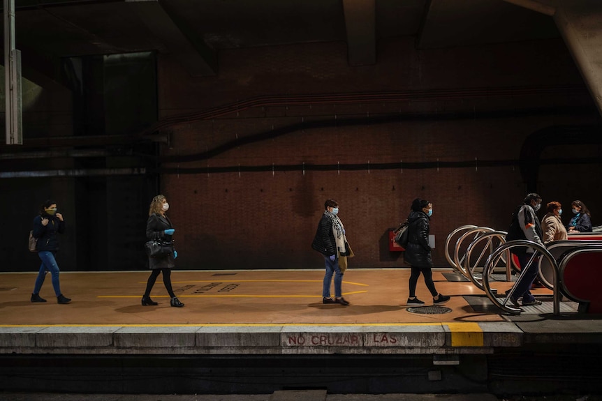 Commuters wearing masks in an underground station in Spain, keeping up social distancing while waiting to board escalators.