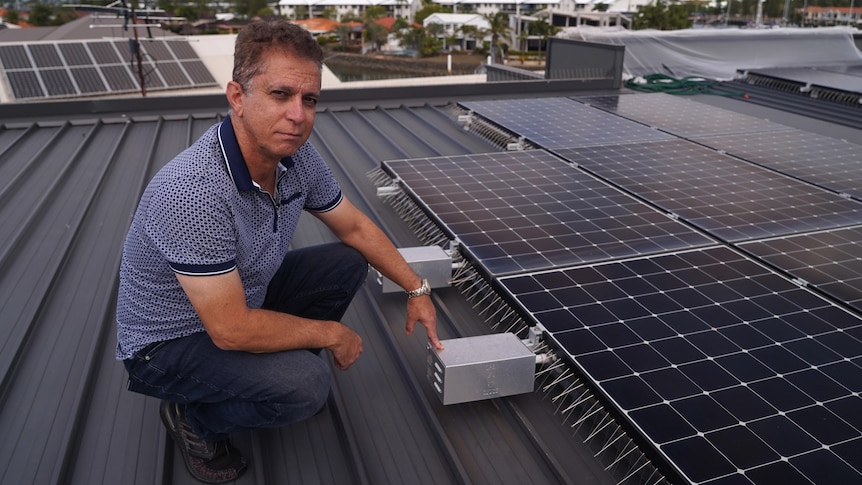 Anthony Parisi wears jeans and a striped shirt while squatting near the solar panels on his roof