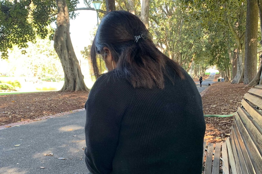 A woman sitting on a park bench from behind.
