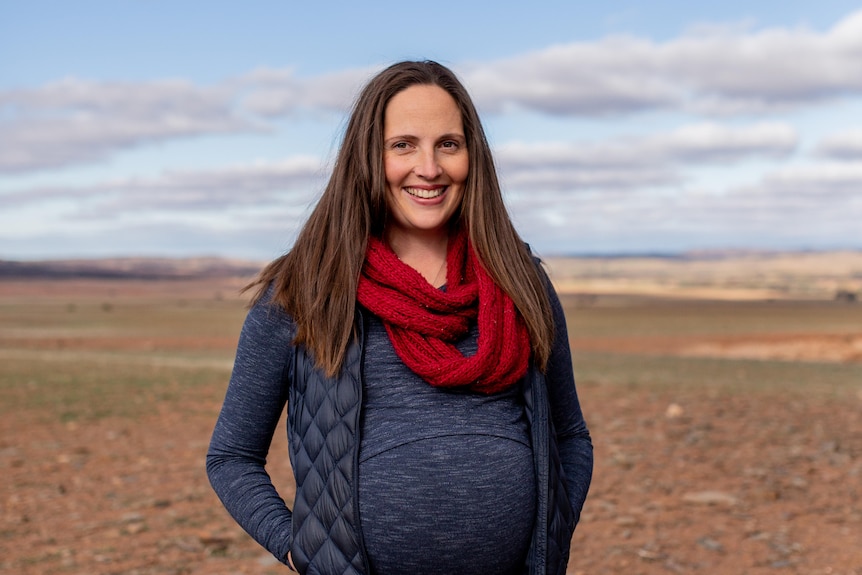 woman with long hair smiling and standing with a open landscape behinf 