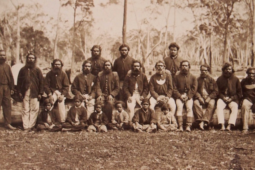 A group of nearly two dozen Indigenous Australians, including children, pose for a photo in bushland