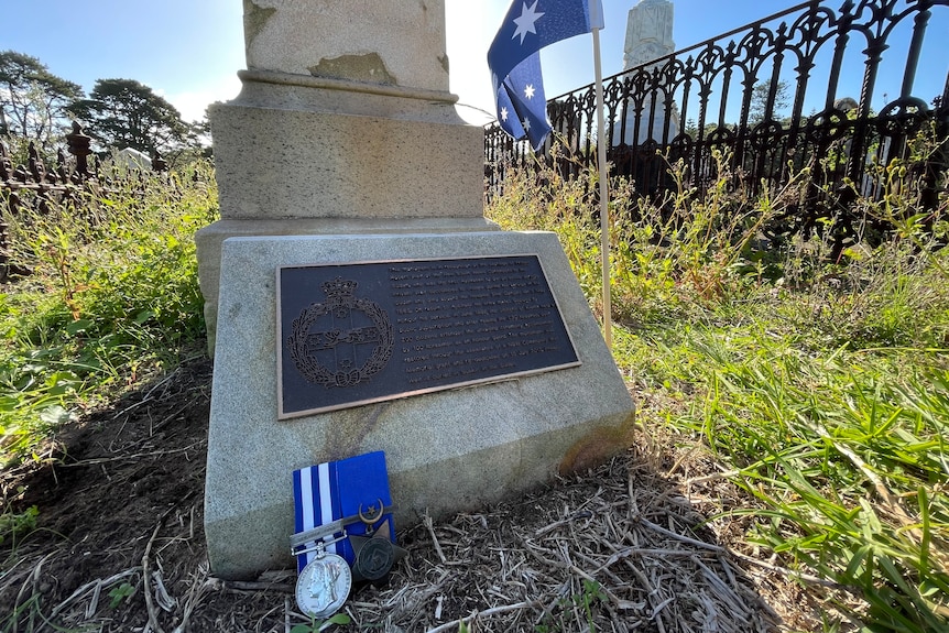Dark plaque on sandstone memorial with service medals