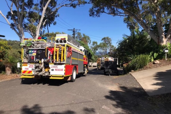 A fire truck parked on the side of a small road with another truck further down the road