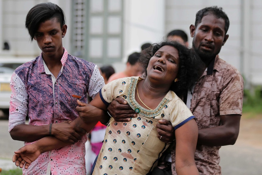 Two men carry a woman who is crying in a blood-stained dress.