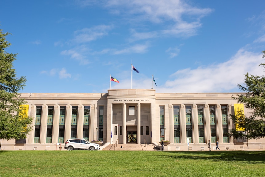 A sandstone building with pillars at the front and three flags on top of it 