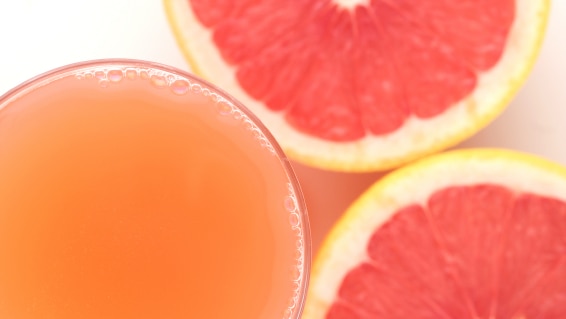 A glass of grapefruit juice and some cut fruit.