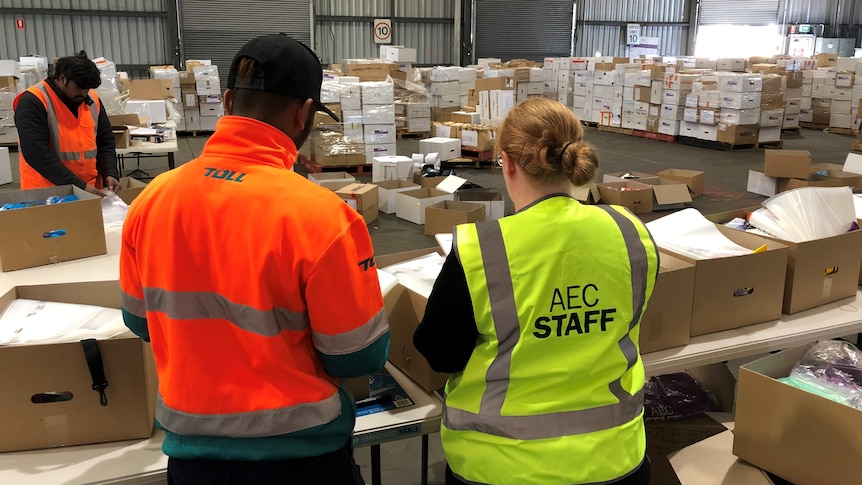 Electoral commission staff and others look over boxes of leftover stationery in a warehouse.