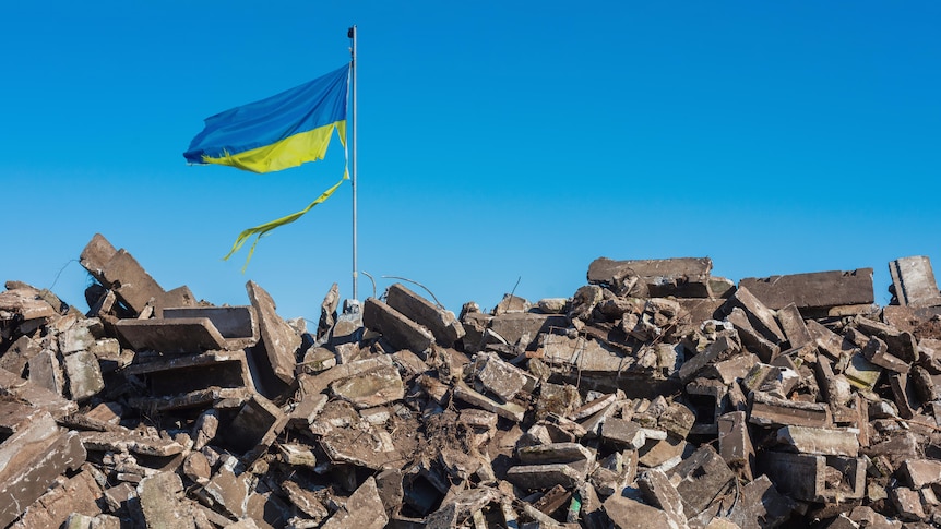 a battered Ukrainian flag on a pile of rubble
