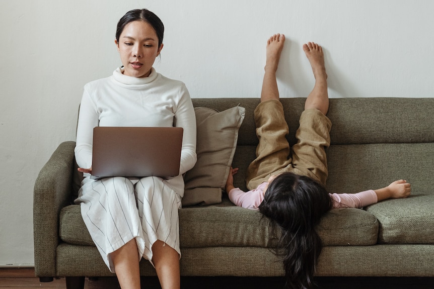 Woman sitting on a sofa working with laptop while child puts feet on wall  