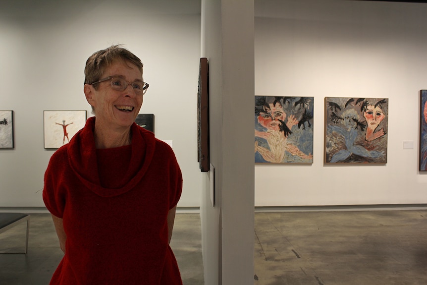 Painter Davida Allen standing inside a gallery space surrounded by paintings.