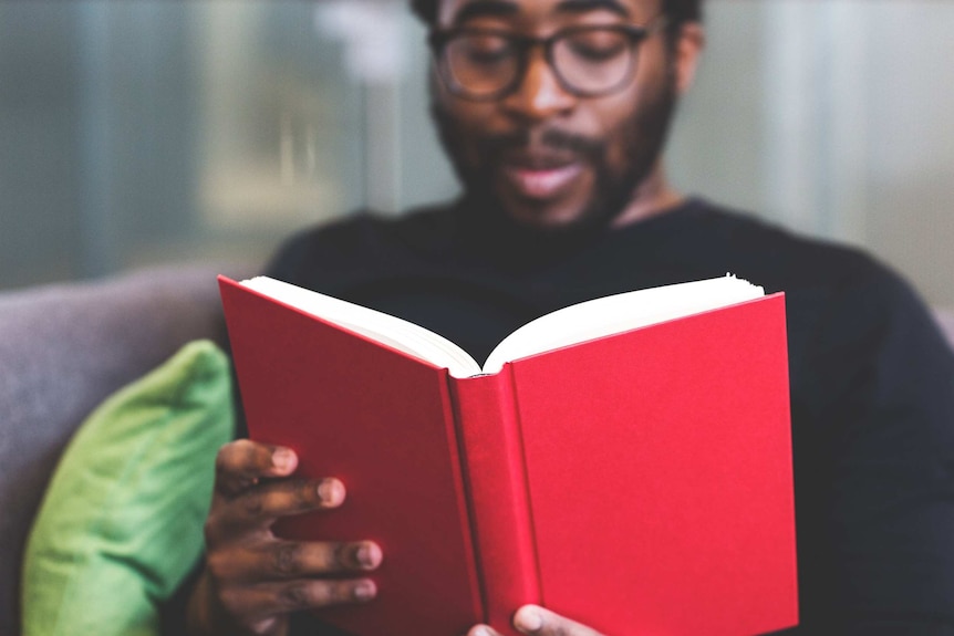 A man reads a book with a red cover.