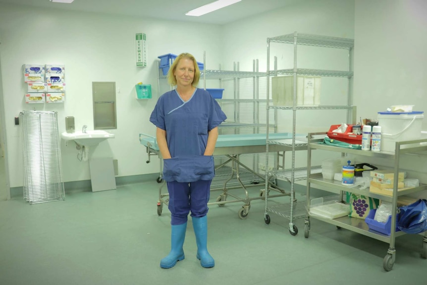Woman stands in gumboots and scrubs in a clinical office environment.
