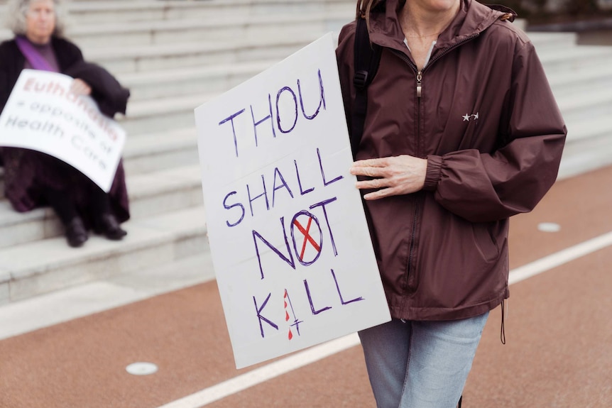 An opponent of voluntary assisted dying holds a protest sign outside WA Parliament.