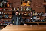 Bearded man Steve Faragi standing in a bar, surrounded by liquor, looking determined.