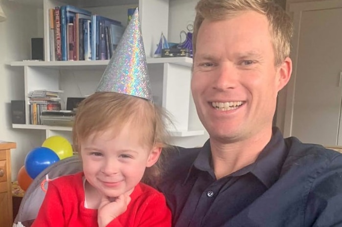 A toddler wearing a party hat sits on her dad's lap