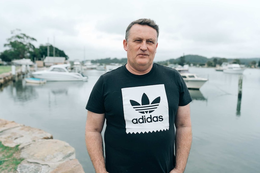 A man in a dark Adidas t-shirt stands in front of a waterway.