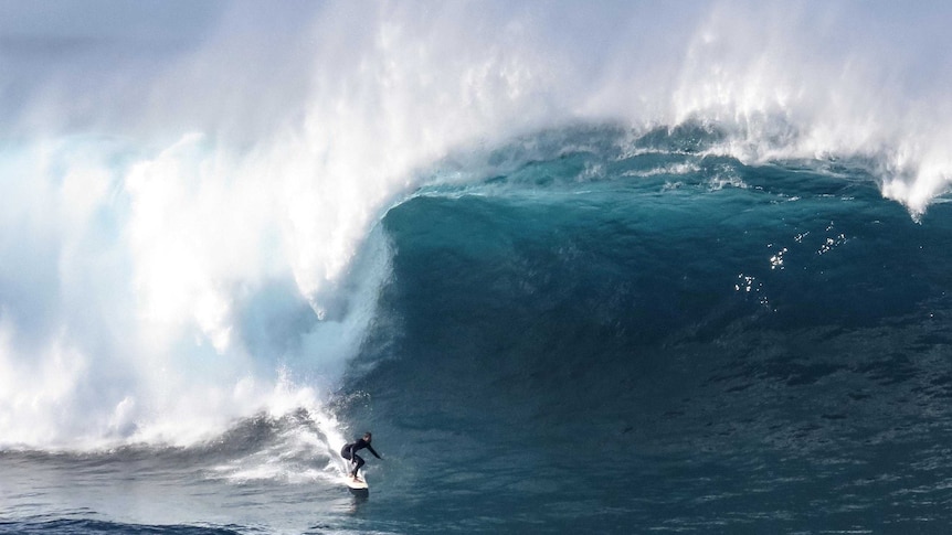 A surfer rides a large wave as it closes in over the top of him.