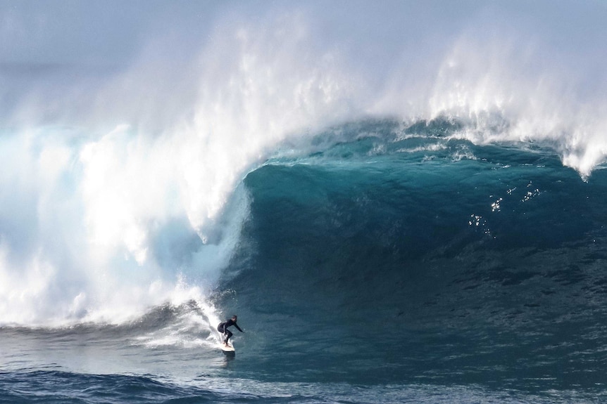 A surfer rides a large wave as it closes in over the top of him.