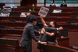 A man holding a sign and a face mask mask is being tackled during a staged protests in Hong Kong.