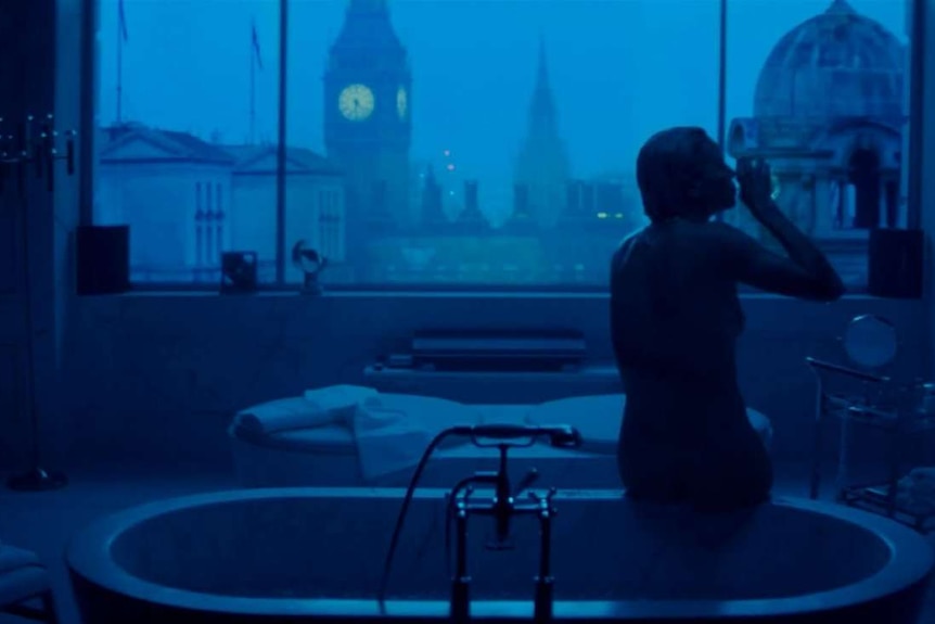 Still image from the film Atomic Blonde, a silhouetted character sitting on the edge of a bathtub at night.