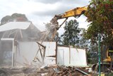 An excavator destroying an old blue wooden home
