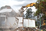 An excavator destroying an old blue wooden home