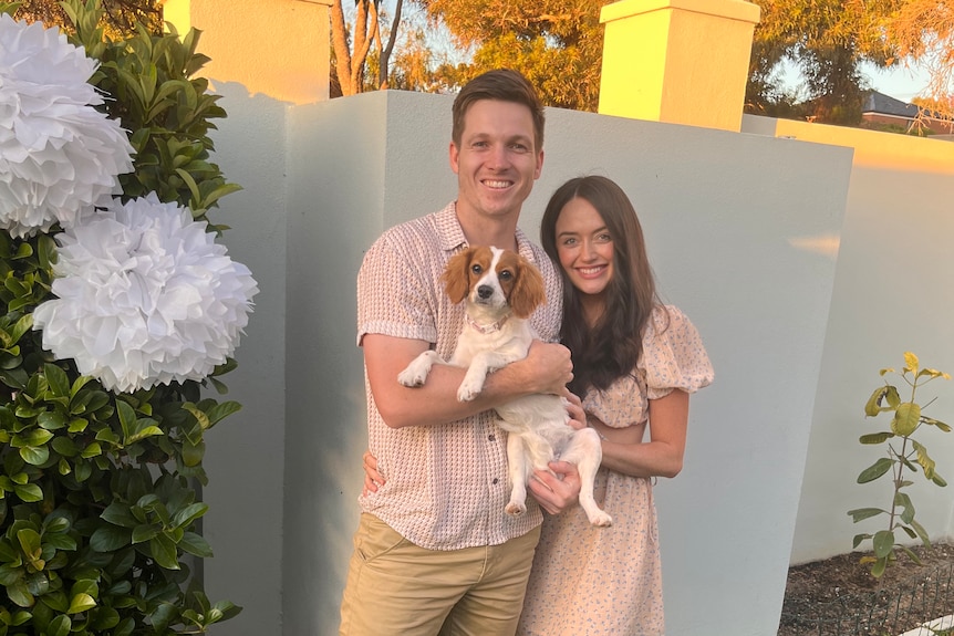 Two people standing together, holding a small dog.