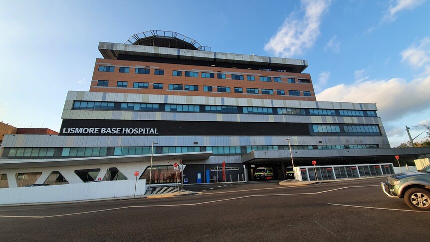 The exterior of Lismore Base Hospital with a helipad on top of a multistorey building and ambulances parked at street level.