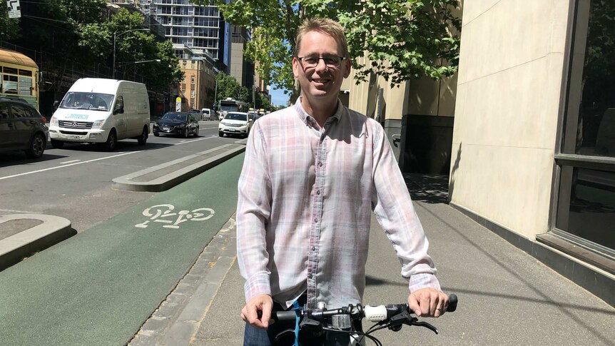 Craig Richards poses with a bicycle on the footpath in Melbourne's CBD. A bike lane is visible in the background.
