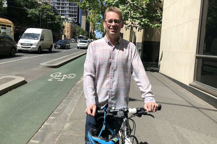 Craig Richards poses with a bicycle on the footpath in Melbourne's CBD. A bike lane is visible in the background.