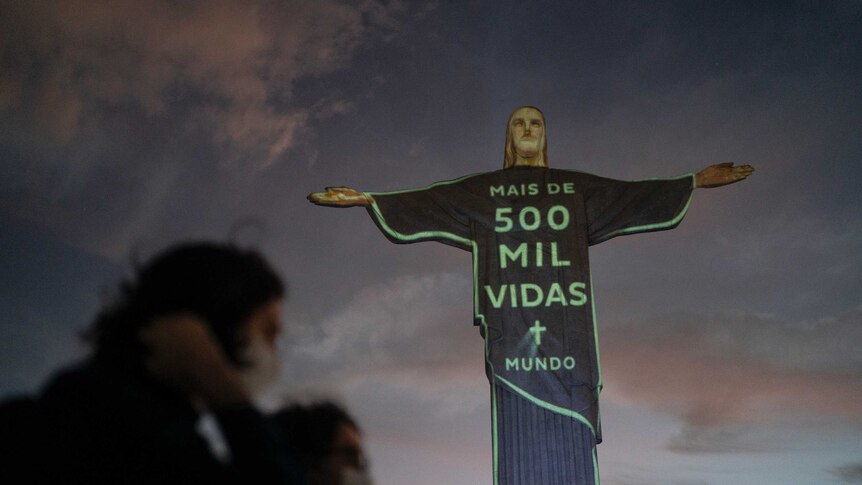 A statue of Jesus Christ statue is lit up with a message in green that reads in Portuguese; "More than 500 thousand lives world"