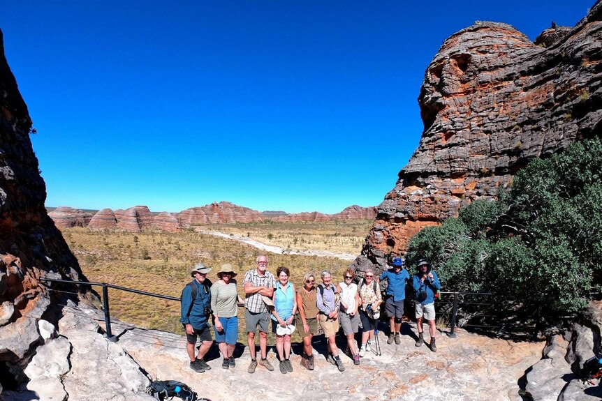 A group of tourists stand in a row in front of a rock formation in the Kimberley.