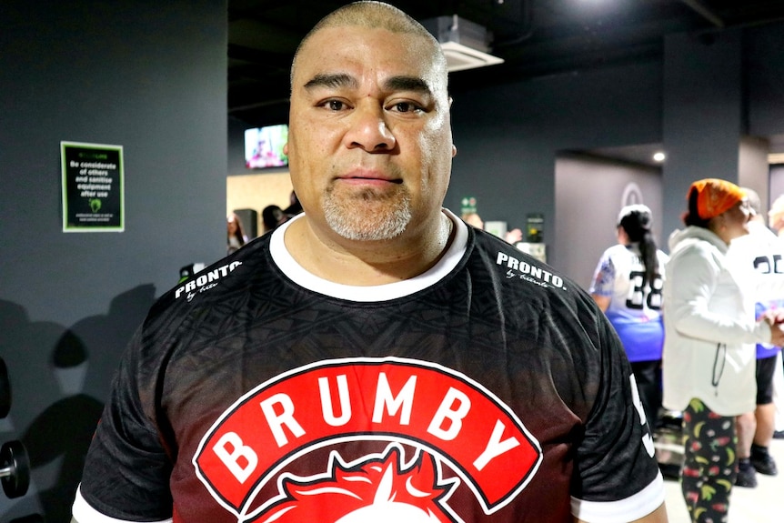 A strong looking Tongan man wearing a Brumby t-shirt looking straight at the camera.