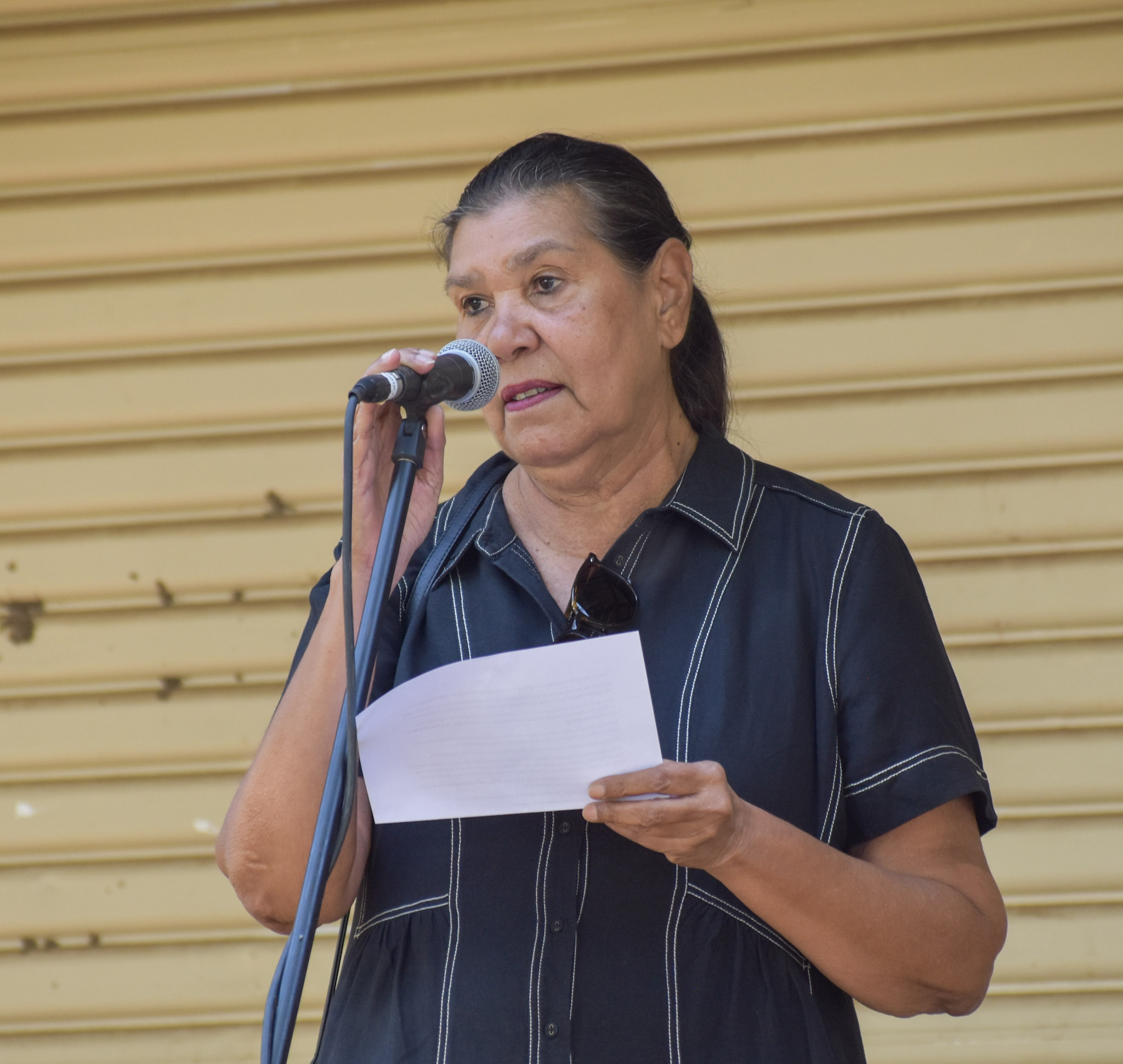 Aboriginal female leader Emily Carter, wearing a black collared shirt, stands in front of a microphone.