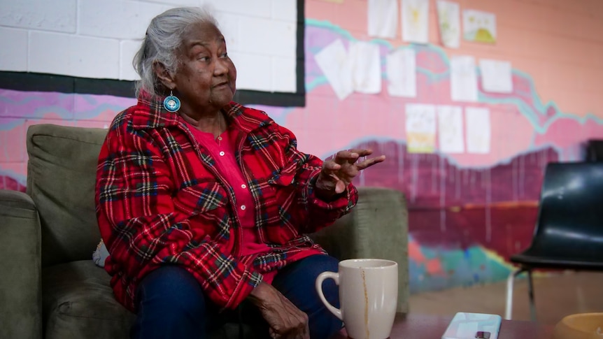 An elderly Aboriginal woman gesticulated while talking in an armchair.