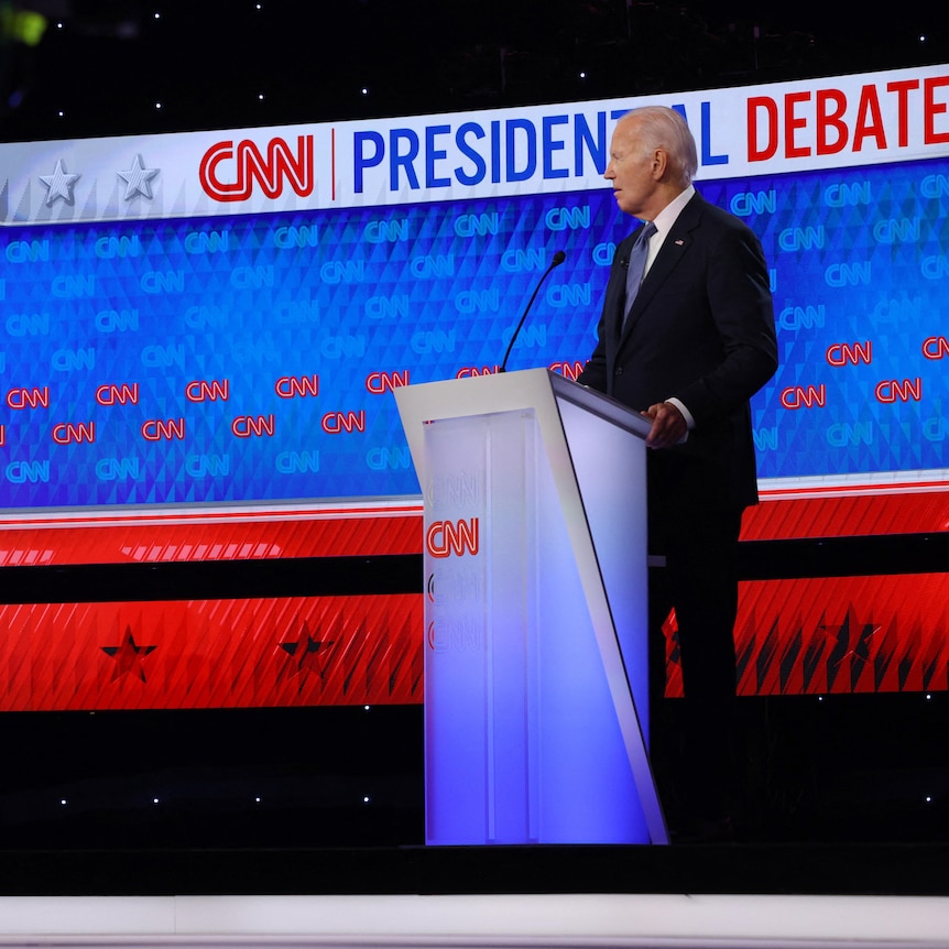 Donald Trump and Joe Biden stand behind branded lecterns on a debate stage in a studio.