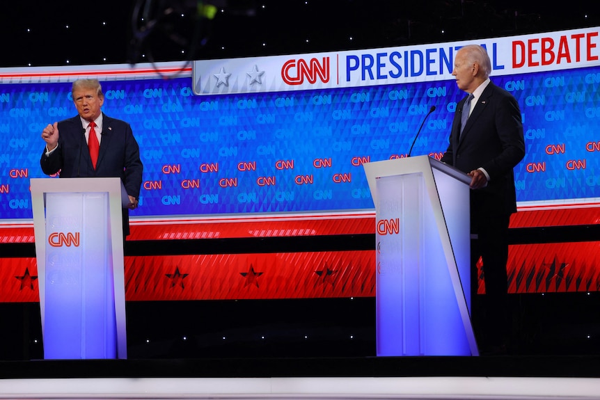 Donald Trump and Joe Biden stand behind branded lecterns on a debate stage in a studio.