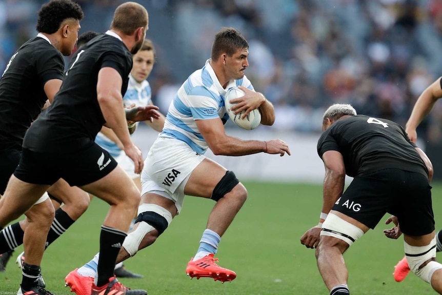 an Argentine player runs with the ball past All Blacks players