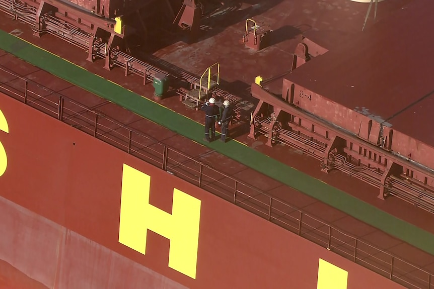 An aerial shot showing two crew members standing on the deck of a bulk carrier.