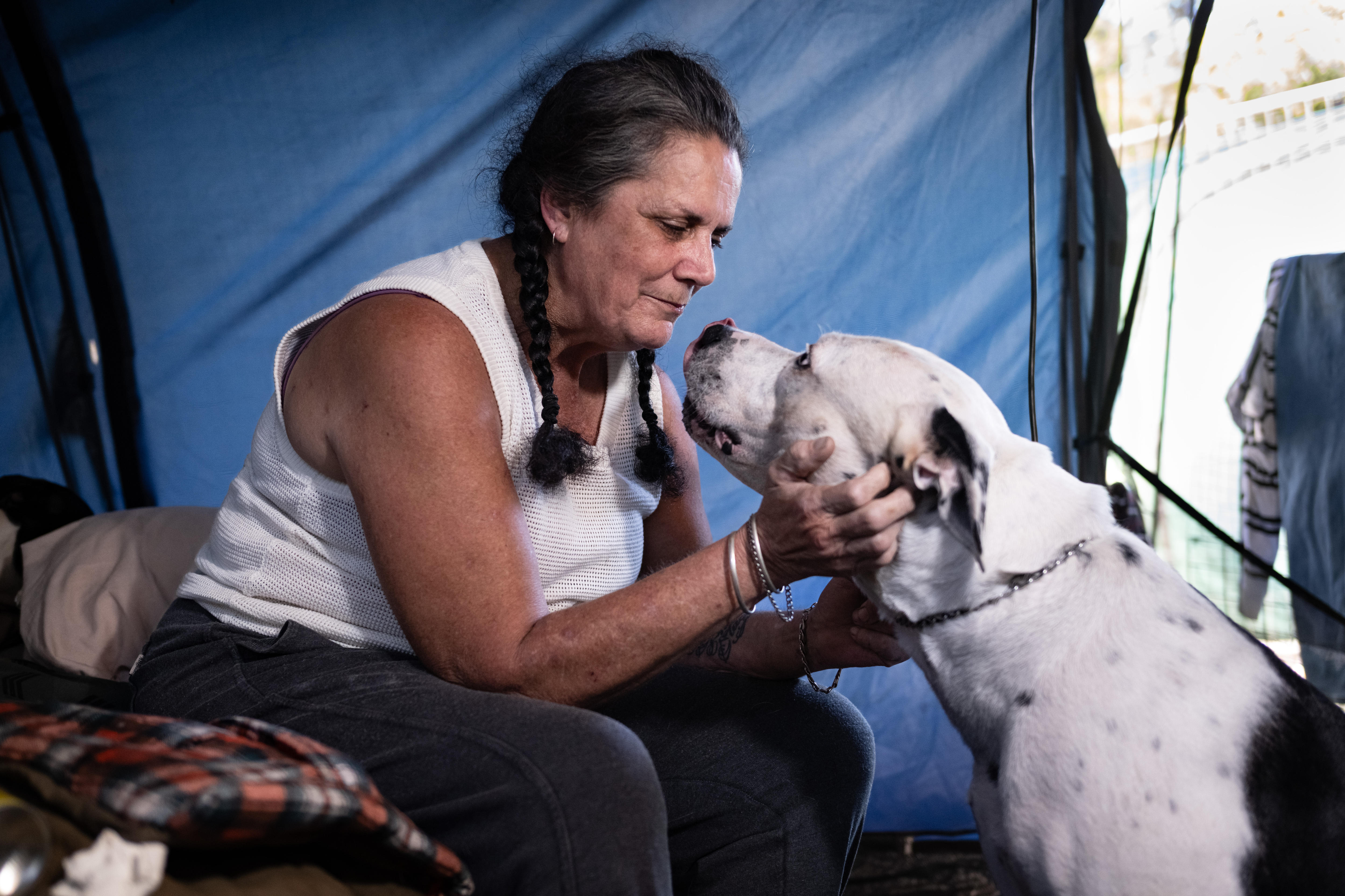 Una mujer de mediana edad acaricia a un perro mientras está sentada en una tienda de campaña.