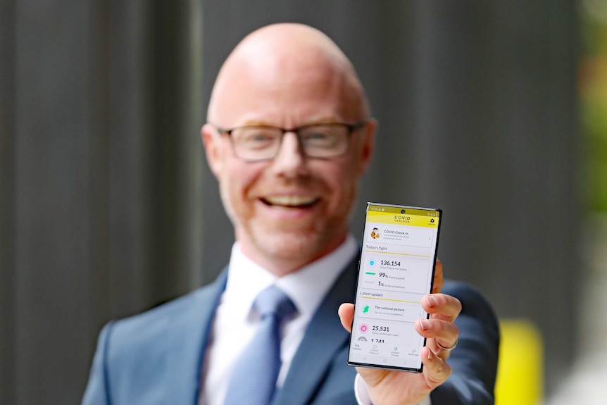 A man holding a smartphone displaying the COVID Tracker App.