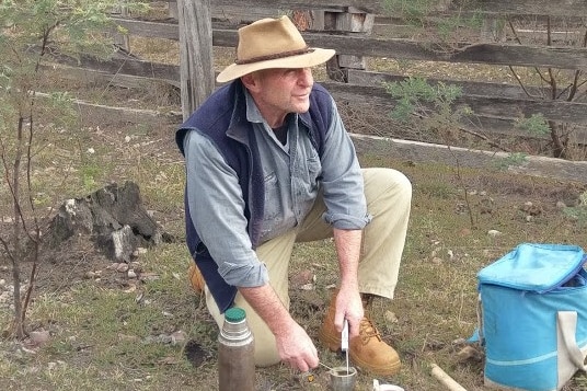 NSW wool grower Robert Ingram kneels on the ground with his lunch as he works in a paddock.