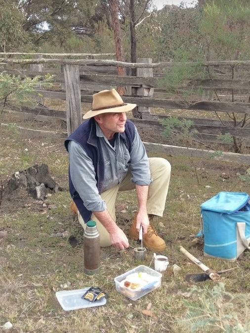 NSW wool grower Robert Ingram kneels on the ground with his lunch as he works in a paddock.