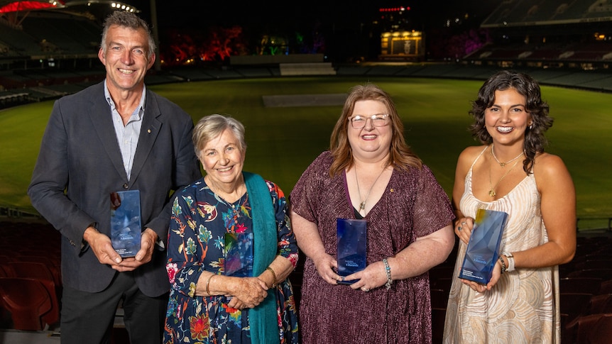 A man and three women posing with their awards in front of an oval