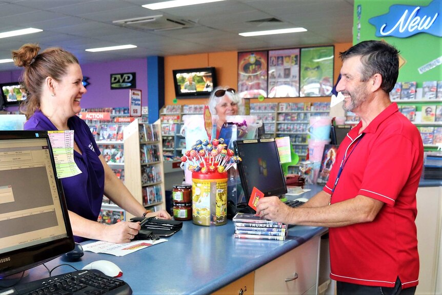 Manager and customer smiling at each other across the counter at a video store.