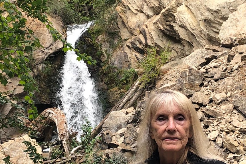 A woman stands in front of a waterfall.