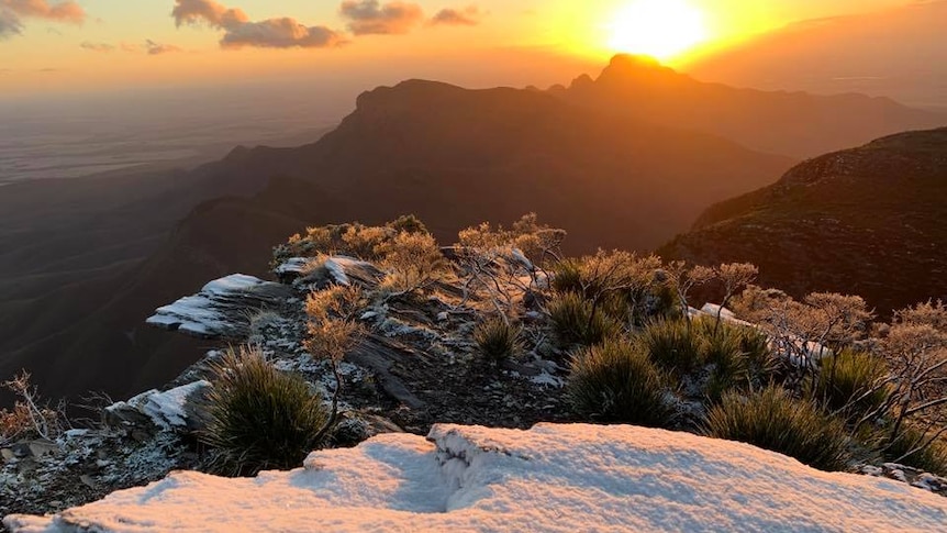 Szerokie ujęcie śniegu na wzgórzu Bluff Knoll, gdy słońce wschodzi nad pasmami Stirlinga.