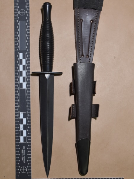 a large black dagger and its leather cover with a ruler on either side